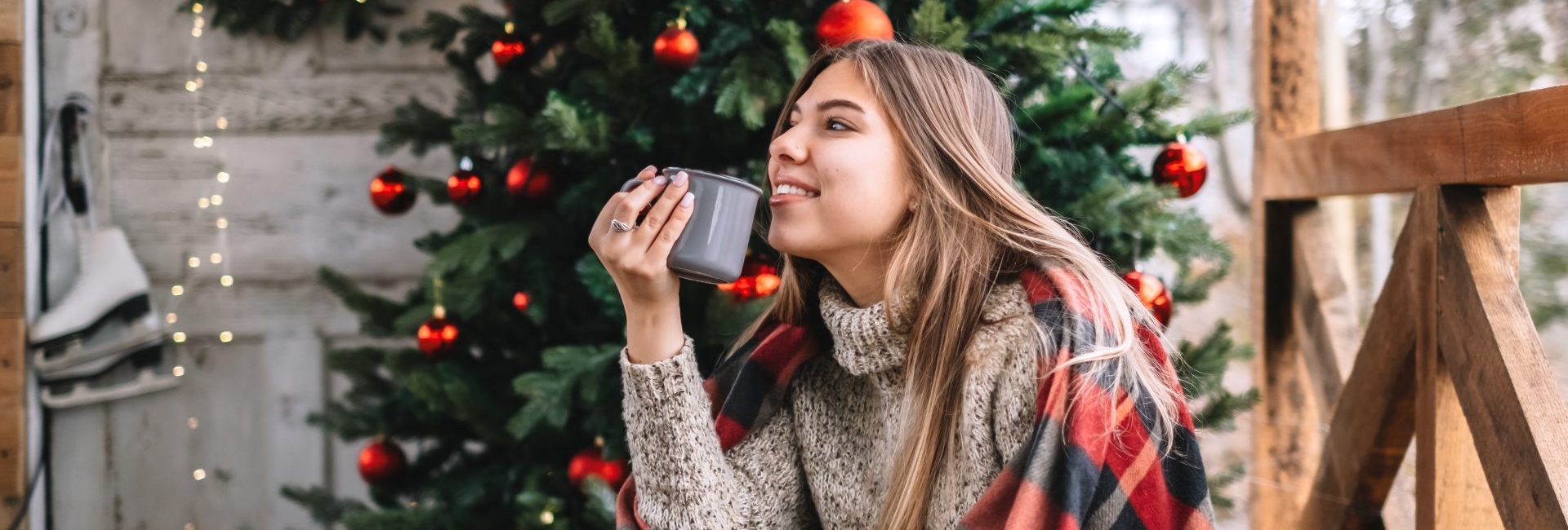 Jeune femme emmitouflée dans un plaid devant un sapin de Noel dans une verandah